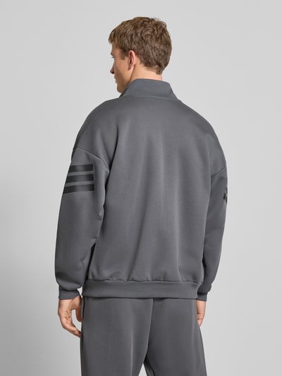 Männermodel trägt Sweatjacke mit Logo und Reißverschluss von adidas Sportswear, Material-Mix, Regular Fit, Rückansicht, gedecktes Grau.