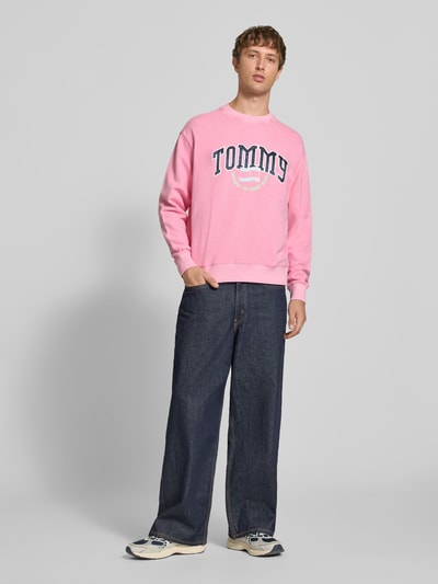 Männermodel trägt Relaxed Fit Sweatshirt aus reiner Baumwolle von Tommy Jeans in Rosa und Blau, Ganzkörperansicht von vorne. Herren Sweatshirt