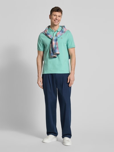 Männermodel trägt Slim Fit Poloshirt mit Logo-Stitching von Gant aus Baumwolle in Mintgrün, Polo-Kragen, kurzärmelig, Ganzkörperansicht von vorne.