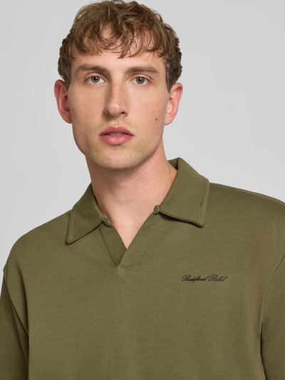 Männermodel trägt Regular Fit Poloshirt mit Logo Modell 'Eddie' von Redefined Rebel, katoenmix, V-hals, logoprint, nahaufnahme oberkörper.