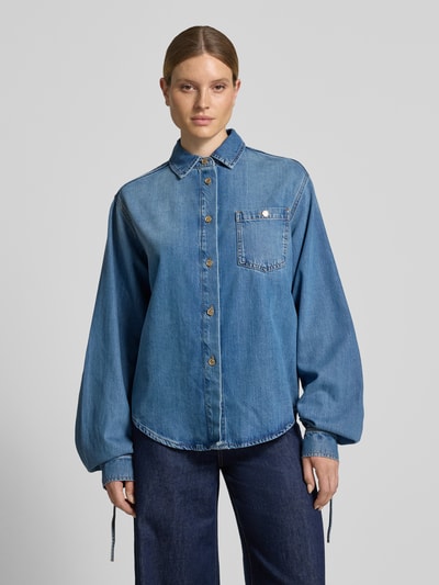 Frauenmodel trägt Oversized Jeansbluse aus Lyocell-Baumwoll-Mix Modell 'JUZY' von Essentiel Antwerp in mittlerem Blau, abgerundeter Saum, Knopfleiste, Ganzkörperansicht von vorne.