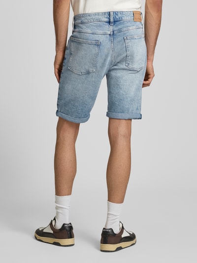 Männermodel trägt Regular Fit Jeansshorts aus Baumwoll-Mix Modell 'RONNIE' von Tommy Jeans in hellblauem Denim mit Label Patch, Ganzkörperansicht Rückansicht.