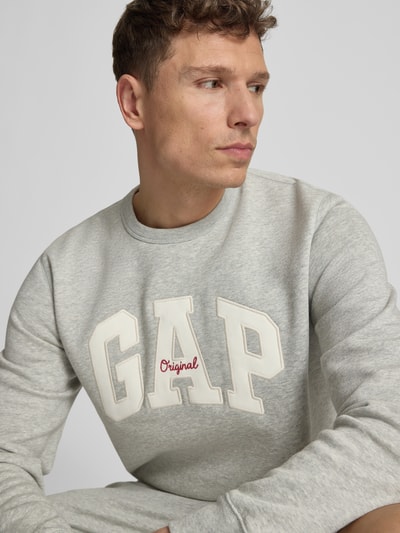 Mannelijk model draagt sweatshirt met logo en ronde hals van GAP, katoenmix, regular fit, grijze stof, nahaufnahme bovenlichaam.