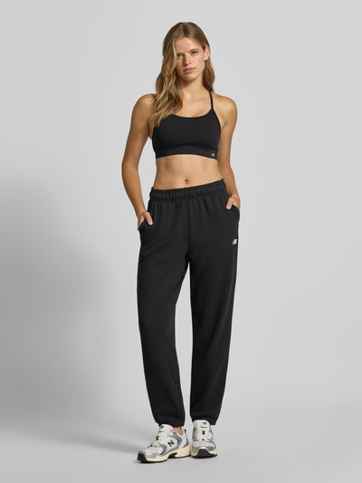 Kobiece model prezentuje Regular Fit Sweatpants mit Logo-Stitching von New Balance, mieszanka bawełny, elastyczny pas, wyhaftowane logo, zakończenia nogawek elastyczne, długość wewnętrzna nogawki w rozmiarze S: 74 cm, krój regular fit, widok całej sylwetki z przodu.