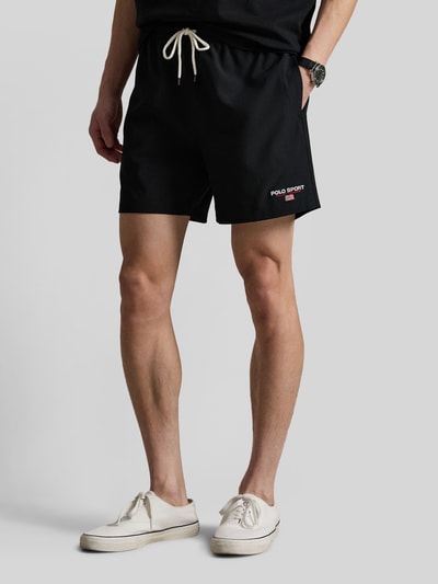 Männermodel trägt Badeshorts mit Label Stitching von Polo Ralph Lauren in Schwarz mit Tunnelzug, elastischem Bund, seitlichen Taschen, Ganzkörperansicht von vorne.
