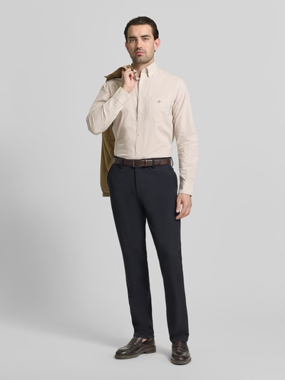 Męski model nosi Slim Fit Freizeithemd mit Logo-Stitching od Gant, jasny beż, lekka bawełna, długi rękaw, widok całej sylwetki z przodu, krój slim fit, logo na piersi, kołnierzyk button-down, kieszeń na piersi, sportowe mankiety, długość pleców w rozmiarze M: 79 cm, szerokość ramion w rozmiarze M: 48 cm, długość rękawa w rozmiarze M: 68 cm.