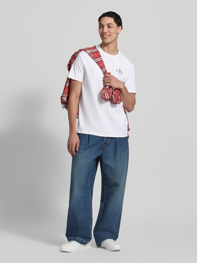Männermodel trägt T-Shirt mit Rundhalsausschnitt und Logo von Calvin Klein Jeans in Weiß, reine Baumwolle, Regular Fit, Ganzkörperansicht von vorne.