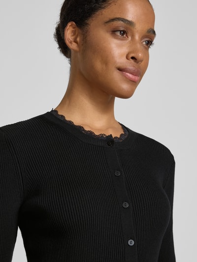 Frauenmodel trägt Slim Fit Strickjacke aus Viskose-Mix Modell 'Wonder' von Vero Moda, Optik: Unifarben, Rippstrick, Spitzen-Besatz, Nahaufnahme Oberkörper.