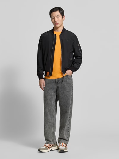 Männermodel trägt schwarze Bomberjacke mit Label-Patch und Eingrifftaschen von Original Bombers, Gerade Passform/Schnitt:, Ganzkörperansicht von vorne. Rückenlänge 67 cm, Schulterbreite 43 cm, Brustweite 53 cm, Ärmellänge 68 cm, Reißverschluss, Reißverschlusstasche am Ärmel, gerippte Abschlüsse, Druckknopfverschluss, klassische Textur.