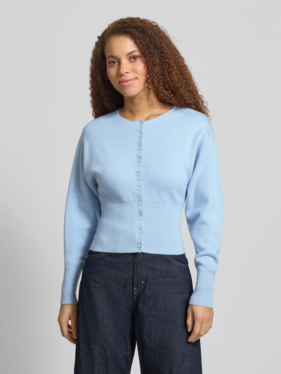 Modelka nosi Slim Fit Cardigan aus Viskose-Mix von Gina Tricot, mieszanka wiskozy, krój regular fit, imitacja dzianiny, listwa guzikowa, okrągły dekolt, szerokie i elastyczne wykończenia, długość tyłu w rozmiarze S: 48 cm, długość rękawów w rozmiarze S: 59 cm, widok całej sylwetki z przodu.