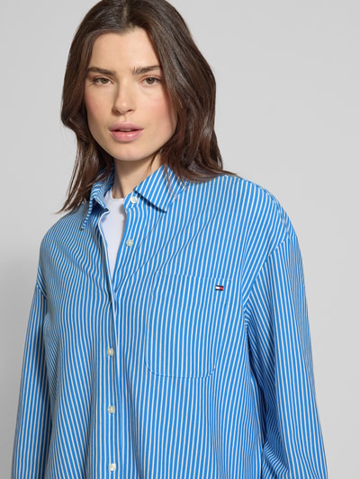 Frauenmodel trägt Oversized Langarmbluse aus Baumwoll-Mix von Tommy Hilfiger in blau-weiß gestreifter Webware mit Logo-Detail, Nahaufnahme Oberkörper.