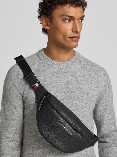Männermodel trägt Bauchtasche mit Strukturmuster von Tommy Hilfiger, robustes Material, Label-Schriftzug, Logo-Details, Nahaufnahme Oberkörper.