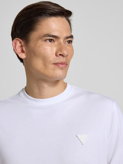 Männermodel trägt T-Shirt mit Logo und Rundhalsausschnitt von Guess, weiß, Baumwoll-Mix mit Modal-Anteil, Relaxed Fit, Nahaufnahme Oberkörper.