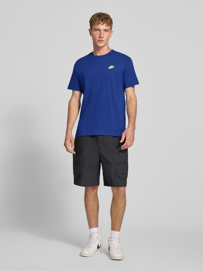 Männermodel trägt Regular Fit T-Shirt aus reiner Baumwolle von Nike in Blau, kombiniert mit dunkler Shorts, Ganzkörperansicht von vorne.