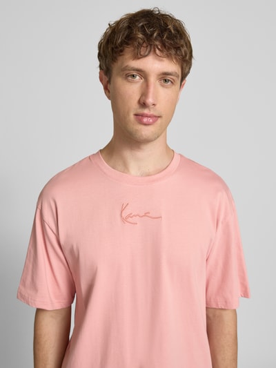 Männermodel trägt Regular Fit T-Shirt mit Logo-Stitching von KARL KANI in Rosa aus Reine Baumwolle, Rundhalsausschnitt, Nahaufnahme Oberkörper, Rückenlänge bei Größe M: 73 cm.