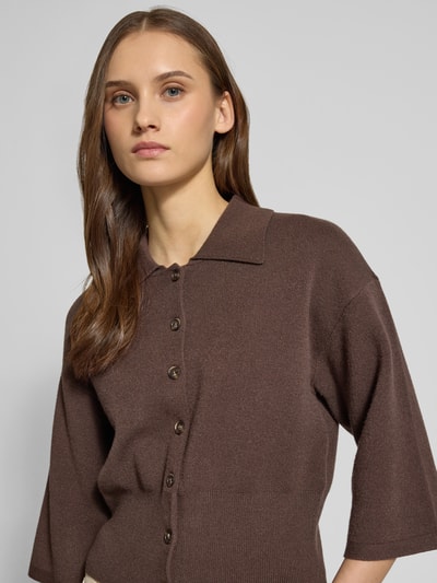 Frauenmodel trägt Strickjacke aus Viskose-Mix Modell 'SHYLA' von Noisy May in Braun mit Umlegekragen, lockere Passform, gerippte Abschlüsse, durchgehende Knopfleiste, 3/4-Arm, Nahaufnahme Oberkörper.