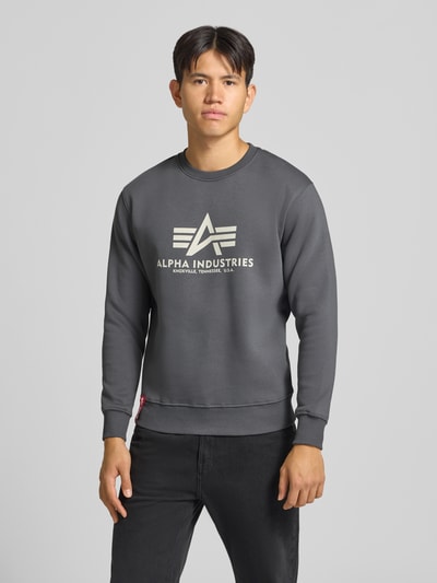 Männermodel trägt Regular Fit Sweatshirt aus Baumwoll-Mix mit Logo-Print von Alpha Industries in Dunkelgrau, Ganzkörperansicht von vorne.