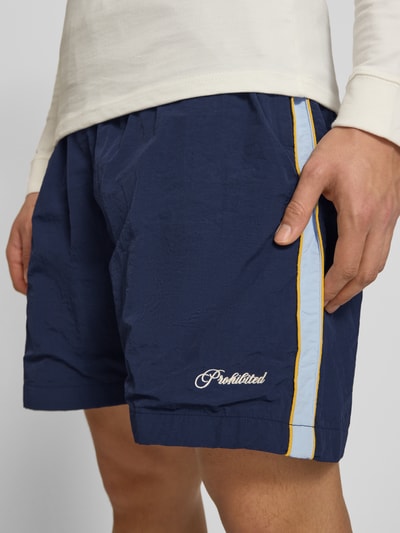 Männermodel trägt Shorts mit Label-Stitching Modell 'Slipstream' von PROHIBITED, dunkelblau mit hellblauen Streifen, Nahaufnahme Oberschenkel, Regular Fit, elastischer Bund