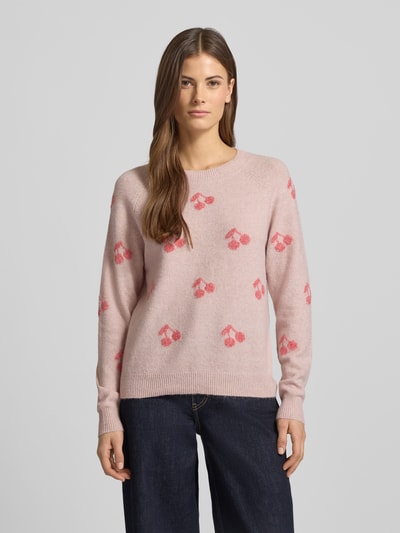 Vrouwenmodel draagt Regular Fit Strickpullover mit Intarsien Modell 'DOFFY INTARSIA' van Vero Moda in lichtroze met allover kersenpatroon, ronde hals, geribde boorden, gebreide textuur, label stitching detail, unicolor look, long sleeves, vooraanzicht volledige lichaamsopname.