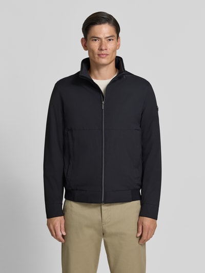 Männermodel trägt Regular Fit Jacke in Stepp-Optik von bugatti, schwarze Farbe, glatte Struktur, Stehkragen, Ganzkörperansicht von vorne.