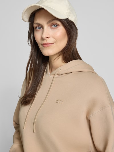 Frauenmodel trägt Oversized Hoodie aus Baumwoll-Mix von Lacoste Sport in Beige mit Logo-Detail, Sweat-Textur, Nahaufnahme Oberkörper.