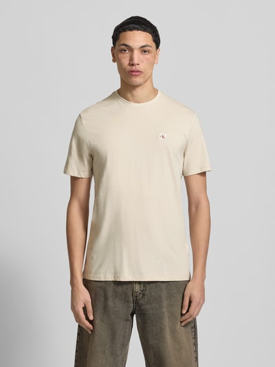 Männermodel trägt T-Shirt mit Label-Badge von Calvin Klein Jeans in Beige, reine Baumwolle, Regular-Fit, Rundhalsausschnitt, Ganzkörperansicht von vorne.