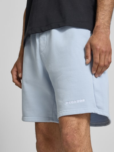 Männermodel trägt Regular Fit Shorts mit Logo-Stitching von Pegador aus Baumwoll-Mix in Hellblau, Nahaufnahme Oberschenkel. Herren Shorts, elastischer Bund, Bundweite 42 cm, Innenbeinlänge 22 cm, Größe M.
