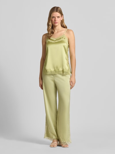 Frauenmodel trägt Flared Fit Stoffhose mit Spitzenbesatz von Gina Tricot in Satin-Optik, hellgrün, elastischer Bund mit Tunnelzug, Ganzkörperansicht von vorne. Damen Stoffhose, Bundweite 40 cm, Innenbeinlänge 79 cm, Größe S.