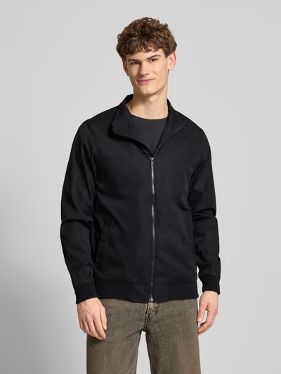 Męski model nosi Regular Fit Kurtkę ze stójką Model 'Hefi' od Blend z bawełny, wpuszczane kieszenie, zamek błyskawiczny, czarna, krój regular fit, długość tyłu w rozmiarze M 71 cm, szerokość ramion w rozmiarze M 46 cm, szerokość klatki piersiowej w rozmiarze M 48 cm, długość rękawów w rozmiarze M 25 cm, elastyczne wykończenia, całe ciało widoczne z przodu