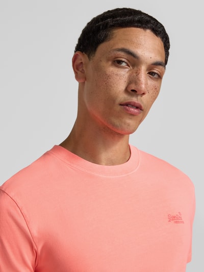 Männermodel trägt T-Shirt mit Rundhalsausschnitt und Label-Stitching von Superdry, Reine Baumwolle, Slim-Fit, Nahaufnahme Oberkörper.