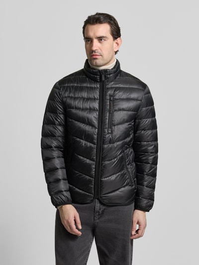 Mężczyznamodel nosi Regular Fit Steppjacke mit Stehkragen od Tom Tailor, czarna, gładka, lekkie pikowanie, elastyczne wykończenia, boczne i piersiowa kieszeń na zamek, funkcja ochrony termicznej, wodoodporność, widok całej sylwetki z przodu.