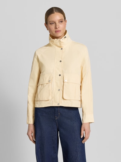 Vrouwenmodel draagt Jacke mit Stehkragen und Pattentaschen van Fuchs Schmitt in regular fit, lichte kleur, grote knopen, recht model, opgestikte klepzakken, tunnelkoord, gladde textuur, maat 36: ruglengte 58 cm, schouderbreedte 41 cm, borstwijdte 54 cm, mouwlengte 63 cm. Vooraanzicht bovenlichaam.