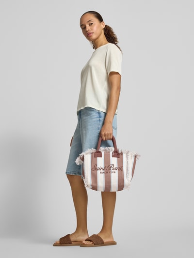 Frauenmodel trägt Handtasche mit Label-Print und Fransen Modell 'COLETTE' von MC2 Saint Barth aus Baumwolle in Braun-Weiß, Ganzkörperansicht von vorne.