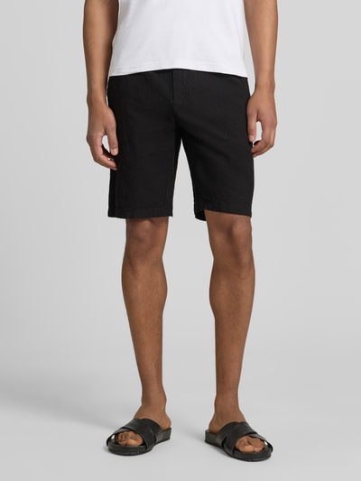 Męski model nosi Bermudas aus Leinen-Mix mit französischen Eingrifftaschen von Lindbergh, czarne, mieszanka lnu i bawełny, krój straight fit, elastyczny pas z trokiem, zapięcie na guzik i zamek błyskawiczny, wpuszczane kieszenie z przodu, kieszenie z tyłu, szerokość w rozmiarze M: 43 cm, długość wewnętrzna nogawki w rozmiarze M: 24 cm, tekstura matowa, gładka, Ganzkörperansicht von vorne.