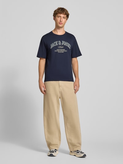 Männermodel trägt Regular Fit T-Shirt aus reiner Baumwolle Modell 'Denver' von JACK & JONES, dunkles Blau, Logo-Print, Ganzkörperansicht von vorne, Rückenlänge 69 cm bei Größe M