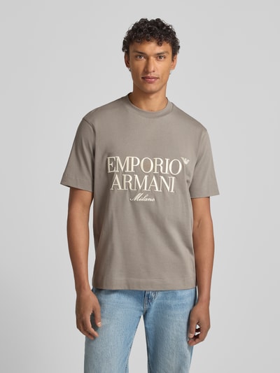 Männermodel trägt T-Shirt mit Label-Stitching von Emporio Armani in Grau, Reine Baumwolle, Regular-Fit, Gerippter Rundhalsausschnitt, Ganzkörperansicht von vorne.