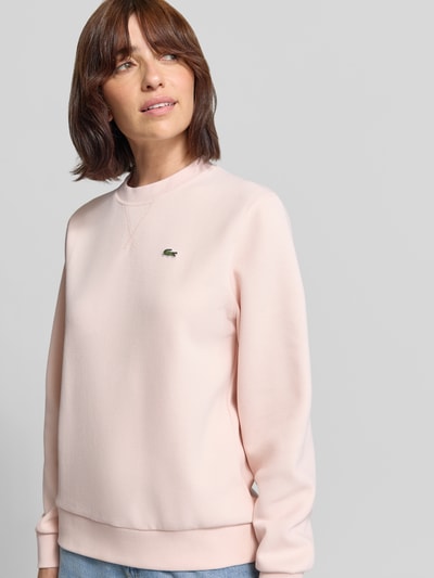 Frauenmodel trägt Relaxed Fit Sweatshirt aus Baumwoll-Mix von Lacoste in zartem Rosa, glatte Struktur, Nahaufnahme Oberkörper. Damen Sweatshirt von Lacoste.