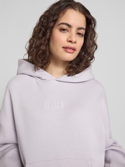 Frauenmodel trägt Relaxed Fit Sweatshirt mit Logo-Print von Review aus Baumwoll-Mix in Helllila, Logo-Stitching, Nahaufnahme Oberkörper.