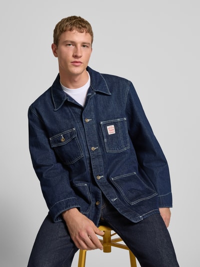 Männermodel trägt Relaxed Fit Jeansjacke mit Logo-Patch Modell 'Berkley' von Levi's® aus dunkelblauer Baumwolle in Nahaufnahme Oberkörper, Jacke mit Umlegekragen, Brust- sowie aufgesetzten Taschen und durchgehender Knopfleiste.