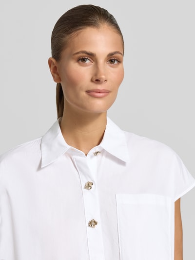 Frauenmodel trägt Knielanges Hemdblusenkleid mit kurzer Knopfleiste von Christian Berg Woman aus Reine Baumwolle, Loose-Fit, Brusttasche, Hemdblusenkragen, feine weiße Struktur, Nahaufnahme Oberkörper.