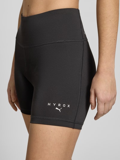 Frauenmodel trägt PUMA x HYROX - Shorts mit Label-Print in Schwarz, körpernaher Schnitt, elastischer Bund, Material-Mix mit Stretch, Nahaufnahme Oberkörper.