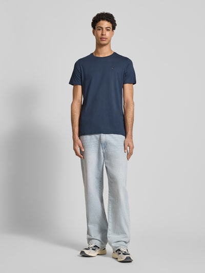 Männermodel trägt T-Shirt in Melange-Optik von Tommy Jeans aus reiner Baumwolle, gerader Schnitt, Rundhalsausschnitt, Logo-Stitching, Ganzkörperansicht von vorne.