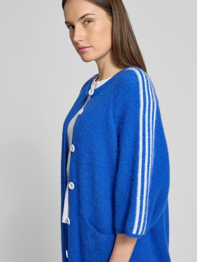 Frauenmodel trägt Strickjacke in Überlänge Modell 'VITOW' von American Vintage in kräftigem Blau mit weißen Knöpfen, gerippte Abschlüsse, 3/4-Ärmel, Rundhalsausschnitt, seitliche Eingrifftaschen, Alpaka-Baumwoll-Mix mit Stretch-Anteil, Nahaufnahme Oberkörper.