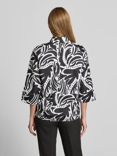 Frauenmodel trägt Bluse mit verdeckter Knopfleiste und 3/4-Arm von Christian Berg Woman aus Reine Baumwolle mit abstraktem Schwarz-Weiß-Muster, Regular-Fit, Hemdblusenkragen, abgerundeter Saum, Rückenlänge 64 cm, Ärmellänge 24 cm, Ganzkörperansicht Rückansicht.
