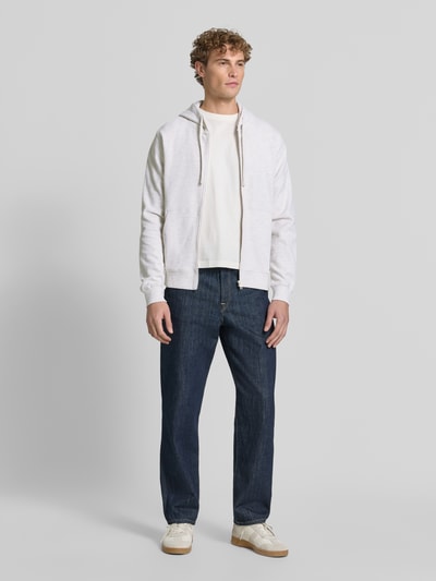 Męski model nosi Relaxed Fit Sweatjacke aus reiner Baumwolle od s.Oliver RED LABEL, jasnobiała bluza rozpinana, ciemnoniebieskie spodnie, jasne buty, gładkie powierzchnie, pełne widoczne barwy, Ganzkörperansicht von vorne.