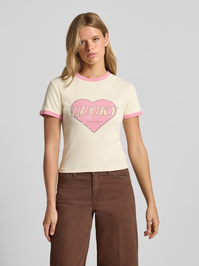 Frauenmodel trägt T-Shirt mit Motiv-Print Modell 'Lucky' von OH APRIL, cremefarben mit rosa Kontraststreifen, Nahaufnahme Oberkörper.