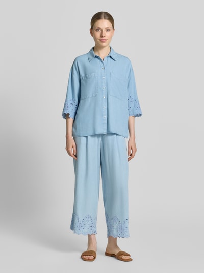 Kobiece model prezentuje bluzka jeansowa 'Jeansbluse mit Lochstickerei und Hemdblusenkragen' od Smith and Soul z lyocellu, krój loose fit, kołnierzyk koszulowy, listwa guzikowa, kieszenie na piersi, haft angielski, długość tyłu w rozmiarze S: 61 cm, długość rękawów w rozmiarze S: 34 cm, widok całej sylwetki z przodu.