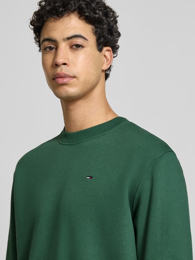 Männermodel trägt Regular Fit Sweatshirt aus Baumwoll-Mix von Tommy Jeans in Optik: Unifarben mit Logo-Stitching, Nahaufnahme Oberkörper.