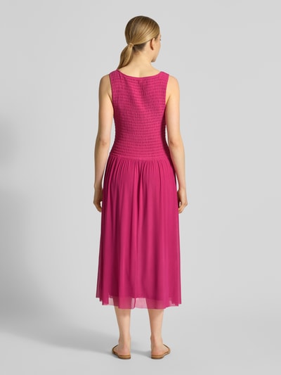 Frauenmodel trägt Midikleid aus Mesh mit Smok-Details von Christian Berg Woman Selection in Pink, fließende Textur, Ganzkörperansicht Rückansicht.