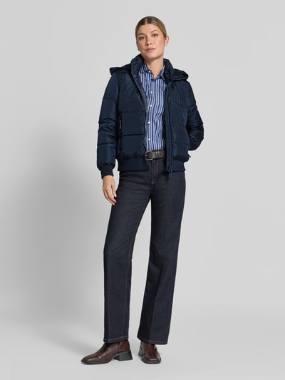 Frauenmodel trägt Steppjacke mit Daunen-Feder-Füllung von Armani Exchange, navyblau, mit Stehkragen, Zweiwege-Reißverschluss, Kapuze, Regular Fit, seitliche Reißverschlusstaschen, elastischer Material-Mix, Kombi zu Hemd und Jeans, Ganzkörperansicht von vorne.
